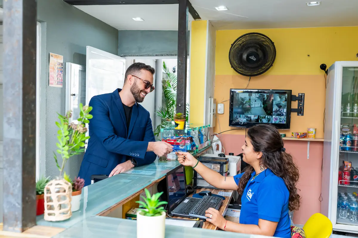 Recepção de hostel em Botafogo com atendente e hóspede fazendo check-in.
