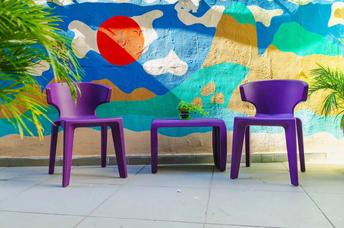 Área externa com cadeiras roxas e mural artístico colorido.