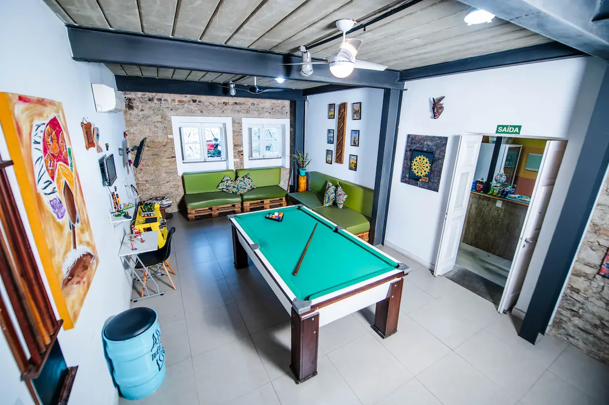 Vista geral da sala de jogos com mesa de sinuca e sofás.